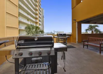 a grill on a patio with a bench and a building at Treasure Island 2102 Beach Front in Panama City Beach
