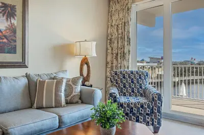 a living room with a couch and a chair and a balcony at Stunning Resort Low Floor Condo! Sleeps 8! Steps 2 Beach & Restaurants! by Dolce Vita Getaways PCB in Panama City Beach