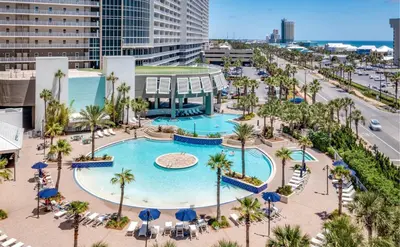 an aerial view of a pool with palm trees and buildings at Stunning Resort Low Floor Condo! Sleeps 8! Steps 2 Beach & Restaurants! by Dolce Vita Getaways PCB in Panama City Beach