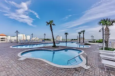 a large swimming pool with palm trees in a resort at Stunning Views! located Steps 2 Beach, Restaurants & Shops! by Dolce Vita Getaways PCB in Panama City Beach