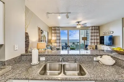 a kitchen with a sink and a living room at Shores of Panama 620-Sleeps 8, Free Fun! Reserved Parking Space! Updated! condo in Panama City Beach