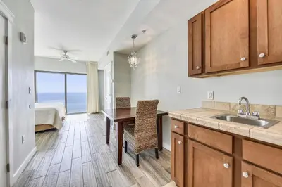 a kitchen with a sink and a table and a bedroom at Origin 1038, Sunset & Gulf View! Perfect for 2! Free Fun! condo in Panama City Beach