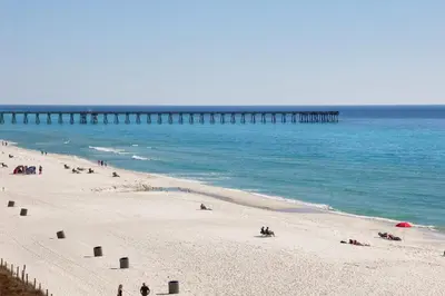a group of people on a beach with a pier at CORNER UNIT! Beach Views! FREE WIFI! 3-Bed, 3-Bath! Sleeps 9! in Panama City Beach