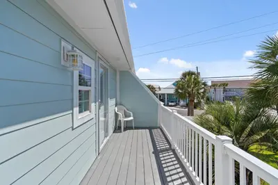 a balcony of a blue house with a chair at 140 Feet To White Sandy Beaches! Newly Renovated! Pool! Grill! in Panama City Beach