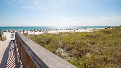 a wooden boardwalk leading to the beach with umbrellas at Stunning 2 BR/2 BA Third Floor Unit Directly On Santa Rosa Beach! Sleeps 6! in Santa Rosa Beach