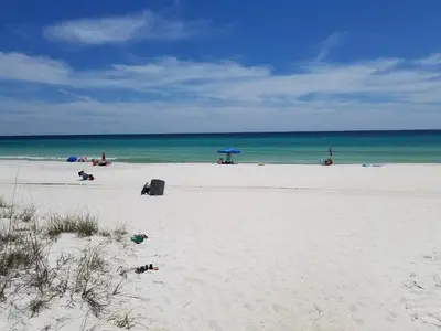 a beach with people laying on the sand and an umbrella at Spacious Waterfront Townhome - Just A Short Walk to Pier Park in Panama City Beach