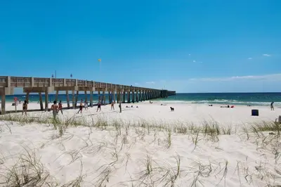 a beach with a pier and people on the sand at Across From The Beach! Near Pier Park & Dining! Sleeps 6! 2 BR / 2 BA! in Panama City Beach