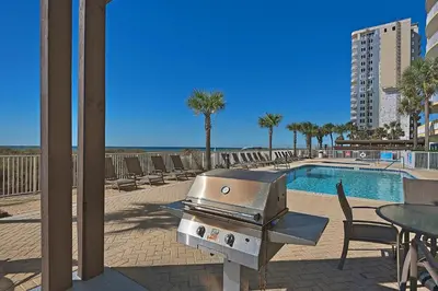 a grill sitting next to a swimming pool with a table and chairs at NEW PROPERTY! Vacation Right on the Gulf in Sand & Seafoam Villa Sleeps 6! in Panama City Beach