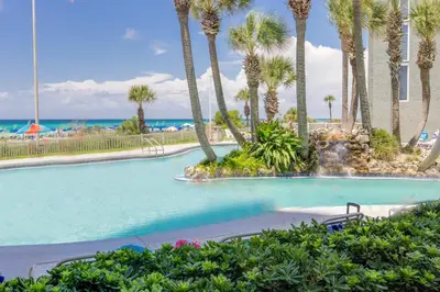 a swimming pool with palm trees and the ocean at Amazing Views! Newly Listed! Family Friendly Unit! Resort Pools! in Panama City Beach