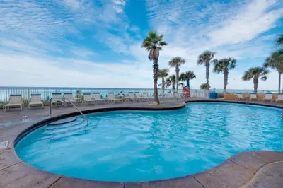 a large swimming pool with palm trees and the ocean at Gulf Front! 2 BR 2 BA! 11th Floor condo + Condo Amenities! in Panama City Beach