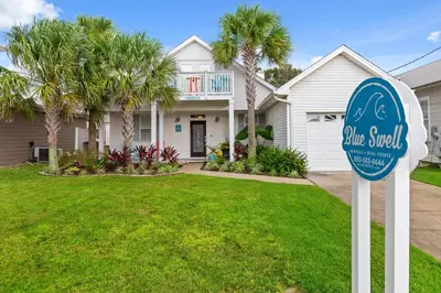 a sign in front of a house with palm trees at Expertly Decorated Family Home, Steps to Beach w/ a Private Heated Pool & Spa! in Panama City Beach