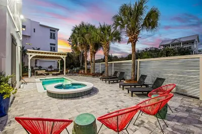 a patio with chairs and a pool and palm trees at 12 Periwinkle Ln - Beach Blessings in Santa Rosa Beach