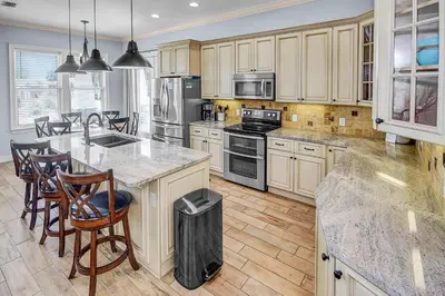 a kitchen with wooden cabinets and a kitchen island with chairs at 5 Bed, 5 Bath Beach Home/Only a 3 Minute Walk To The Beach! SLEEPS 12 in Panama City Beach