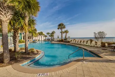 a swimming pool with palm trees and chairs next to the ocean at Luxury Beachfront Condo w/ 2 Balconies! Sleeps 8! Walk to Pier Park! in Panama City Beach