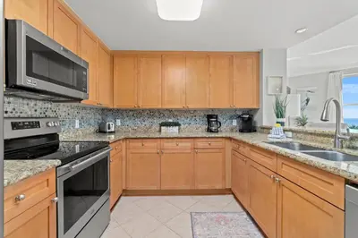 a kitchen with wooden cabinets and stainless steel appliances at Luxury Beachfront Condo w/ 2 Balconies! Sleeps 8! Walk to Pier Park! in Panama City Beach