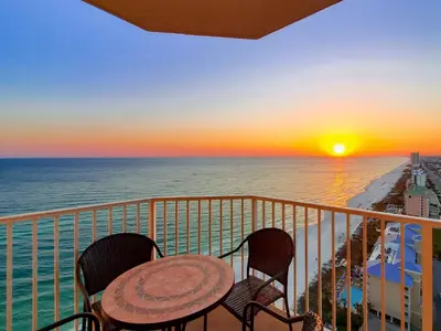 a table and chairs on a balcony with a sunset at End Unit - Directly On The Gulf! Sleeps 6! Italian Luxury Furnishings! in Panama City Beach