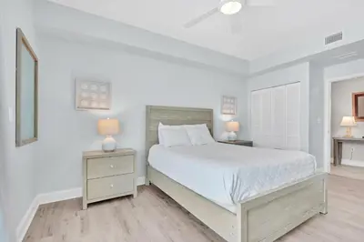 a white bedroom with a bed and two lamps at Aqua Resort 811 in Panama City Beach