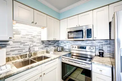 a kitchen with white cabinets and stainless steel appliances at Walkable Panama City Beach Condo with Pool Access! in Panama City Beach