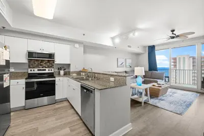 a kitchen with white cabinets and a living room at Modern Beachfront Condo on the Beach Sleeps 6! by Dolce Vita Getaways PCB in Panama City Beach