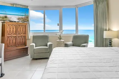 a bedroom with a bed and two chairs and the ocean at Top of the Gulf 825 in Panama City Beach
