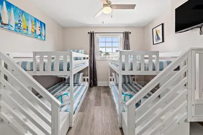 a bedroom with two bunk beds and a tv at Welcome to Dolphin Fun B, BRAND NEW Duplex Walk to the Beach in Panama City Beach