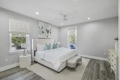 a white bedroom with a bed and a chair at La Joya Azul in Inlet Beach