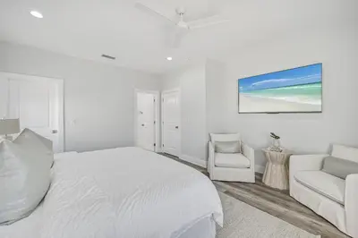 a white bedroom with a bed and a chair at La Joya Azul in Inlet Beach