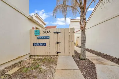 a wooden gate with a sign on it next to a building at 2 BR townhome w/private patio, beach access, 4 communal pools, hot tub, mini golf, tennis, & more! in Panama City Beach