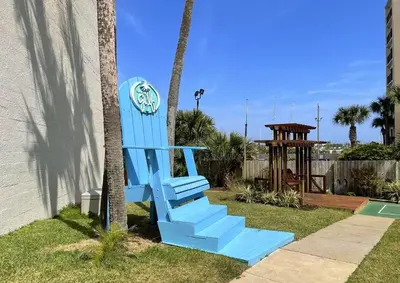 a blue chair sitting next to a palm tree at Top of the Gulf 808- Gulf Coast Getaway in Panama City Beach
