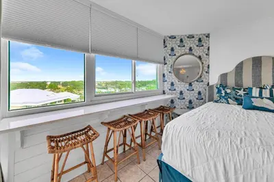 a bedroom with a bed and some chairs and windows at Top of the Gulf 808- Gulf Coast Getaway in Panama City Beach