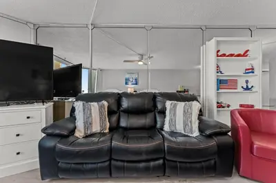 a living room with a black leather couch and a red chair at Top of The Gulf 306 in Panama City Beach
