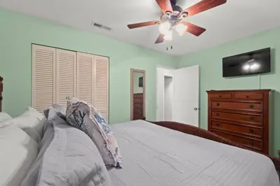 a bedroom with a bed with a ceiling fan and a dresser at Paradise Found in Panama City Beach