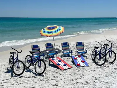 four bikes and chairs on a beach with an umbrella at Lifestyles & Dreams in Santa Rosa Beach