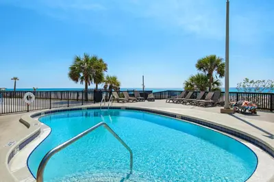 a swimming pool with chairs and the ocean in the background at Sunbird 709W Beach Life in Panama City Beach