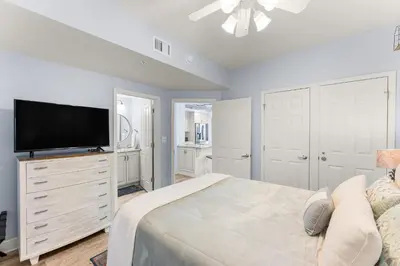 a white bedroom with a large bed and a flat screen tv at Celadon 209 in Panama City Beach