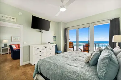 a bedroom with a bed and a balcony with the ocean at Treasure Island #0303 in Panama City Beach