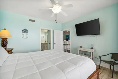 a bedroom with a white bed and a flat screen tv at Treasure Island #1005 in Panama City Beach
