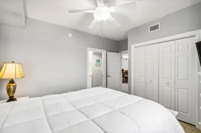a white bedroom with a large white bed and a ceiling fan at Treasure Island #1808 in Panama City Beach