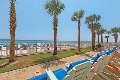 a row of blue chairs and palm trees on a beach at Huge Balcony - Beachfront - Renovated - FLPCB87 in Panama City Beach